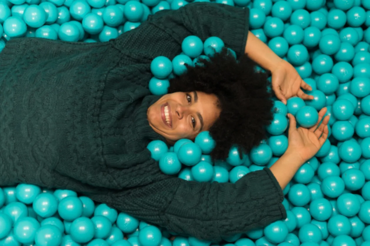 woman of color in turquoise ball pit kidulting concept